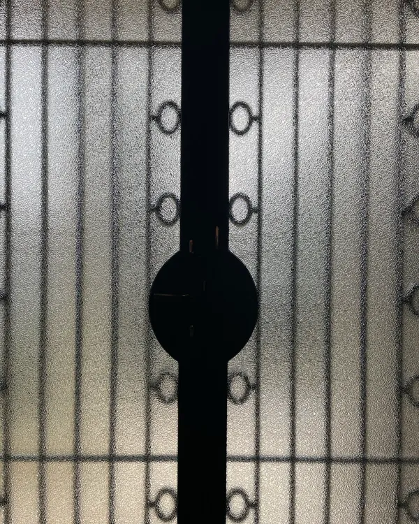 Détail en gros plan d'une porte métallique vitrée, montrant le verre texturé rétroéclairé et la silhouette noire du mécanisme de serrure
